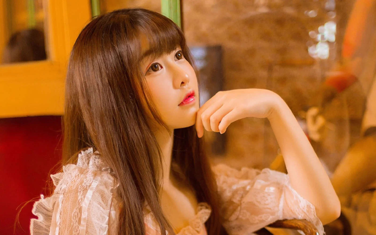 一名长发女性在暖色室内光线下侧脸托腮看向镜头。