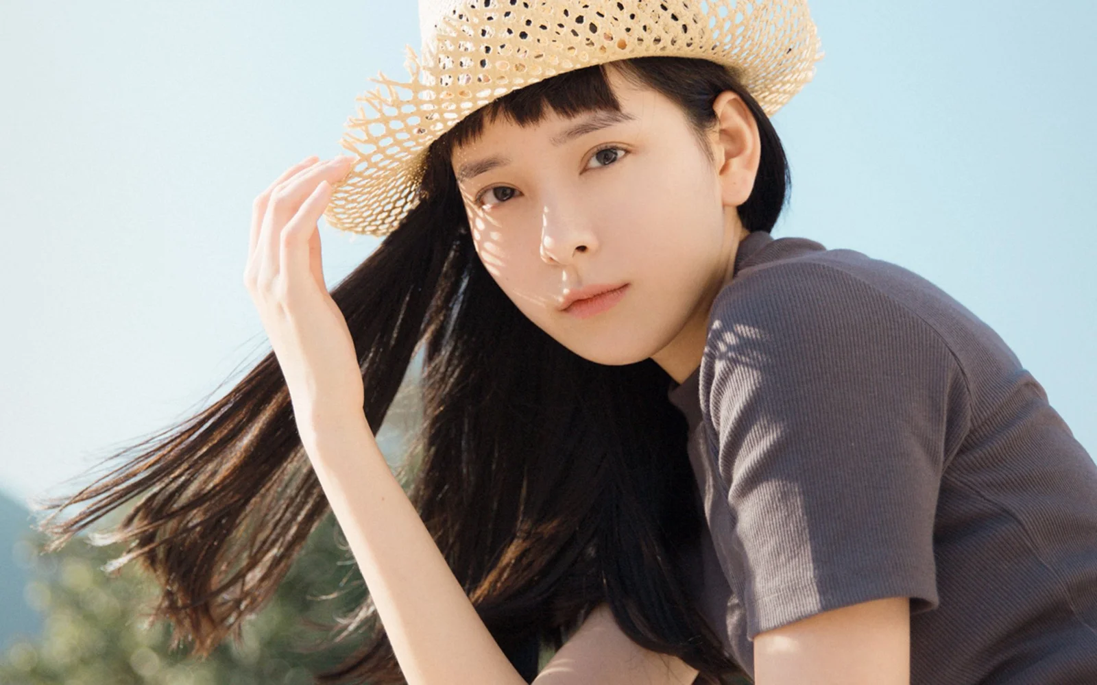 一名戴草帽的長髮女子在戶外陽光下看向鏡頭。