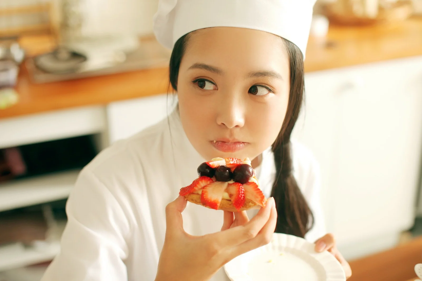 白いコック帽をかぶった女性がイチゴのデザートを手にして横を見ている。
