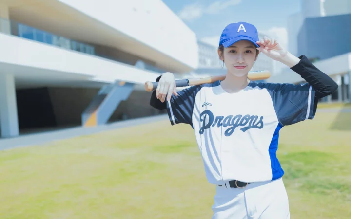 一名身穿棒球服、手持球棒的女子站在户外建筑前。