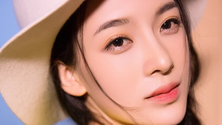 つばの広い帽子をかぶった成人女性の顔を大きく捉えた、明るい瞳と柔らかなメイクが印象的なポートレートです。