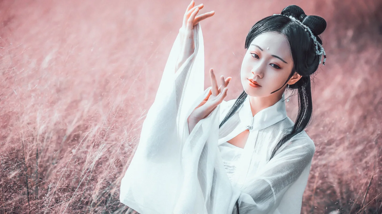 一名身穿白色传统服饰的女子在粉色草地前摆出优雅姿态。