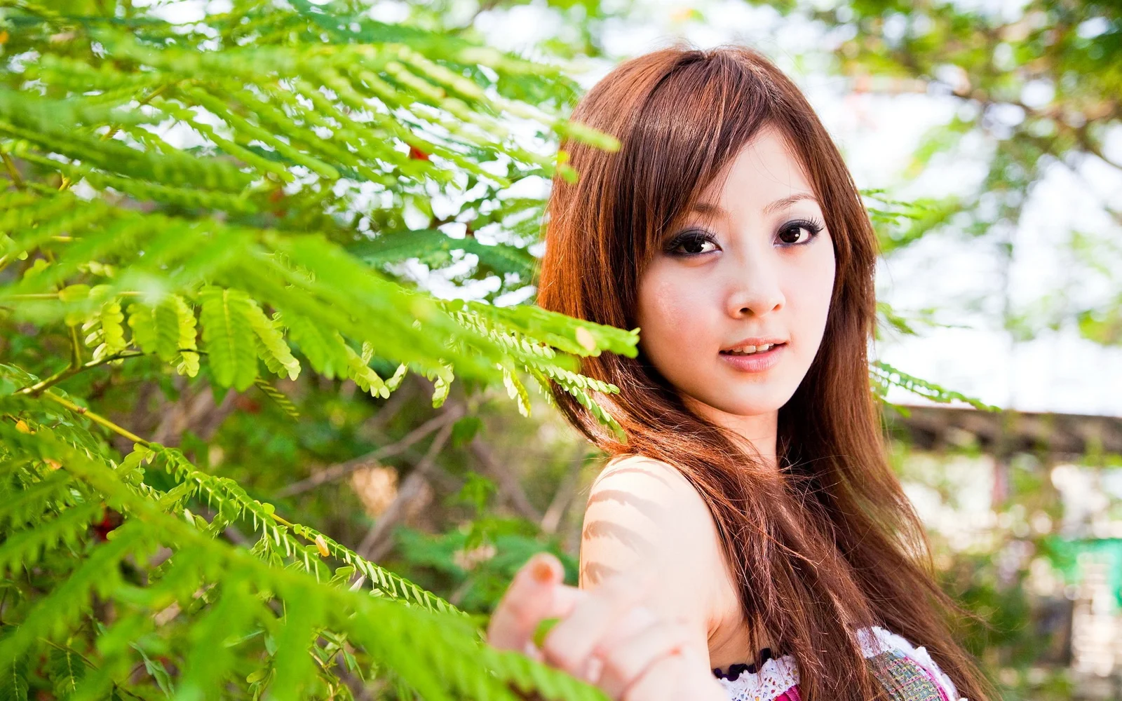 一名成年女性站在绿叶间，面向镜头微笑。
