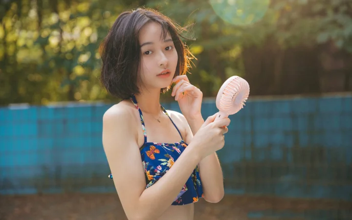 一名成年女性在户外阳光下手持小风扇面对镜头。