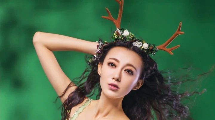 一名成年女性戴著鹿角與花卉頭飾，在綠色背景前擺姿勢。