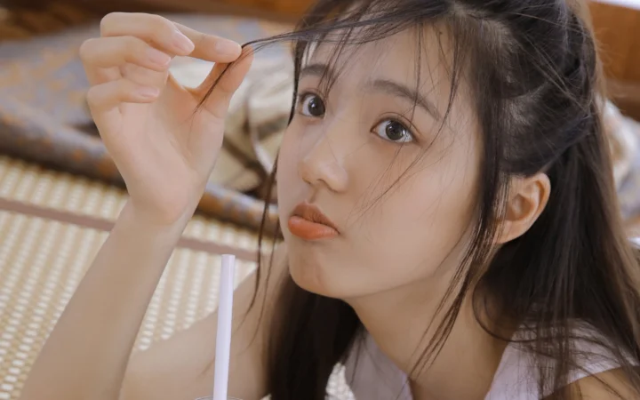 一名女性近距离看向镜头，手指轻轻捏起脸旁的一缕头发。