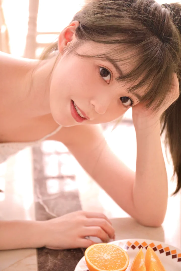 따뜻한 햇빛 아래 한 여성이 오렌지 조각 옆에서 카메라 가까이 얼굴을 기울이고 있습니다.