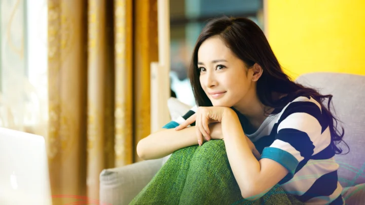 一名成年女性坐在窗边的沙发上微笑看向镜头。