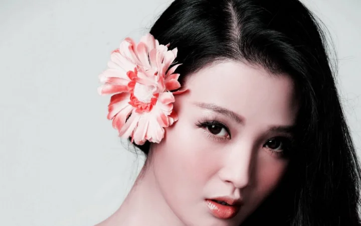 一名黑髮女性近距離面向鏡頭，耳旁佩戴著一朵粉色花朵。