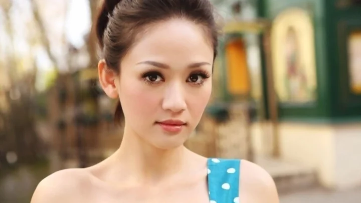 青いノースリーブのトップスを着た成人女性が、屋外でカメラに向かっています。
