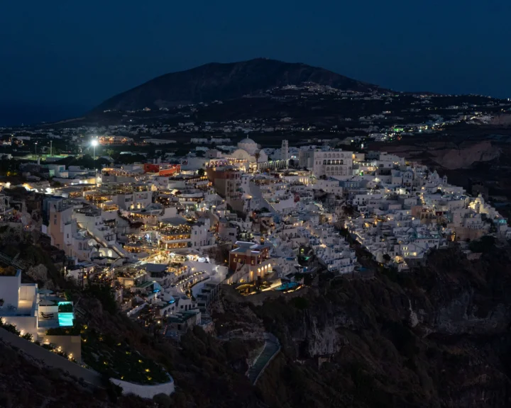 夜幕下，山坡上的白色建筑群灯火通明，远处是深色山体。