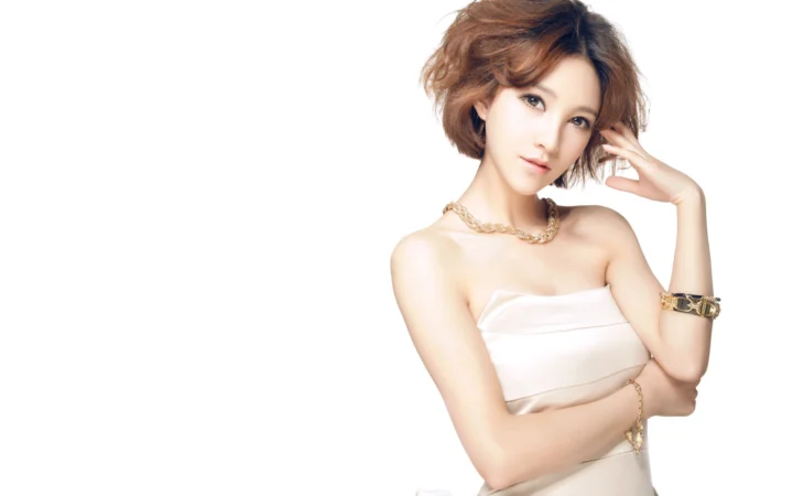 흰색 끈 없는 상의를 입은 짧은 머리 여성이 흰 배경 앞에서 포즈를 취하고 있습니다.