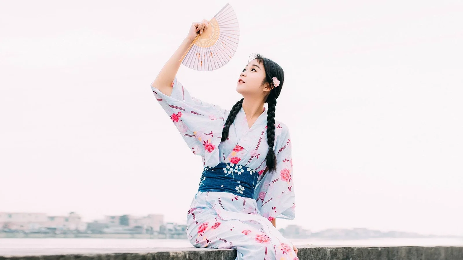 淡い花柄の浴衣を着た女性が、扇子を持って水辺に座っている。