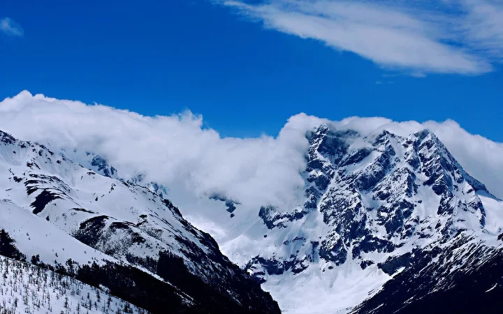 蓝天下，积雪覆盖的山峰被云层环绕，呈现壮丽的高山景色。