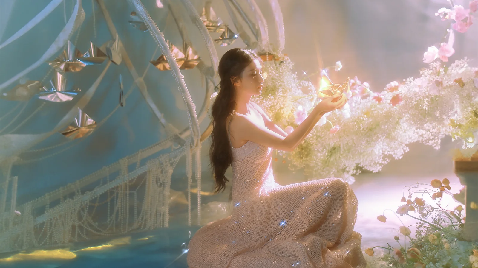きらめくドレスを着た成人女性が、幻想的な花飾りと柔らかな光の中に座っています。