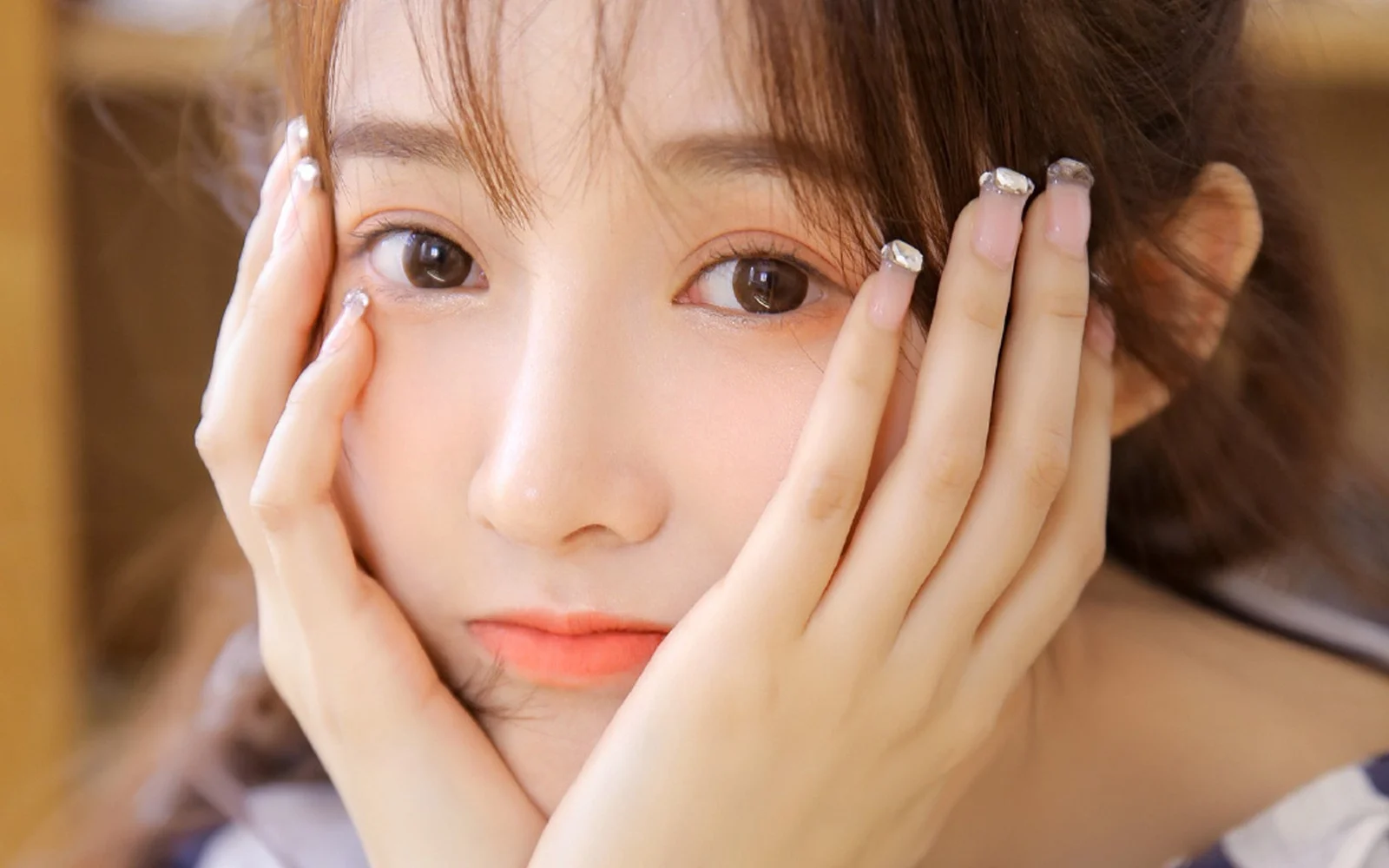 한 여성이 카메라를 바라보며 양손으로 얼굴을 부드럽게 감싼 클로즈업 인물 사진이다.