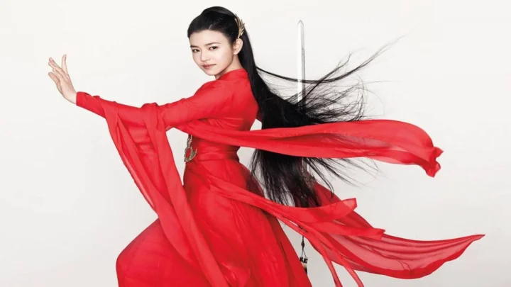 一名身穿红色飘逸长裙、留着长发的女子站在白色背景前。