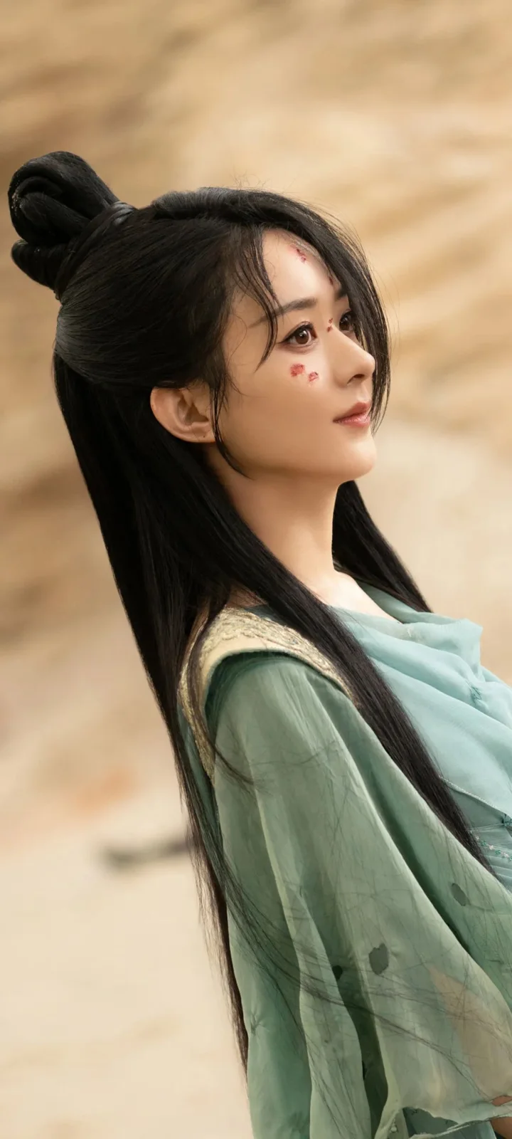 一名身穿绿色服装、留着长发的女性侧身望向一旁，背景为暖米色。