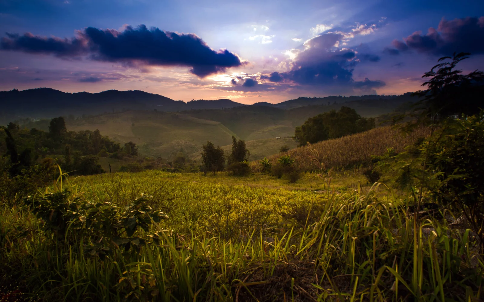 夕阳穿过云层，照亮了起伏的山丘和前景田野。