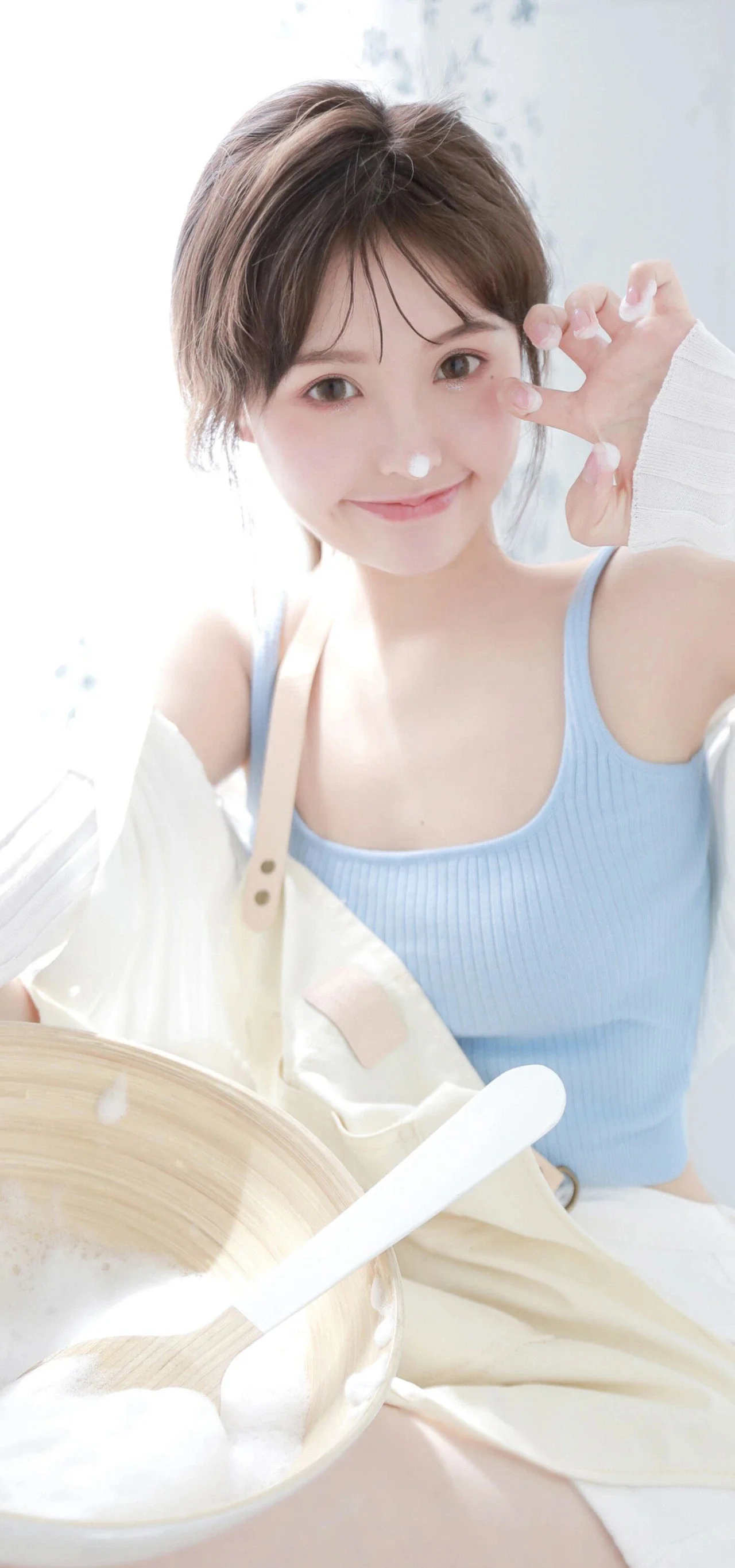 一名女性穿着浅蓝色背心，手持勺子坐在甜点前对镜头微笑。