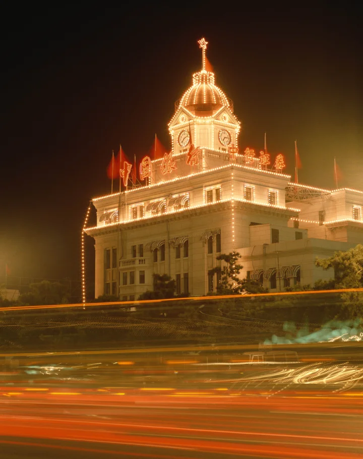 夜色中一座灯光璀璨的建筑矗立在道路旁，前景车流形成明亮的光轨。