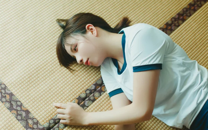 一名女子穿著白色藍邊上衣側躺在編織墊上。