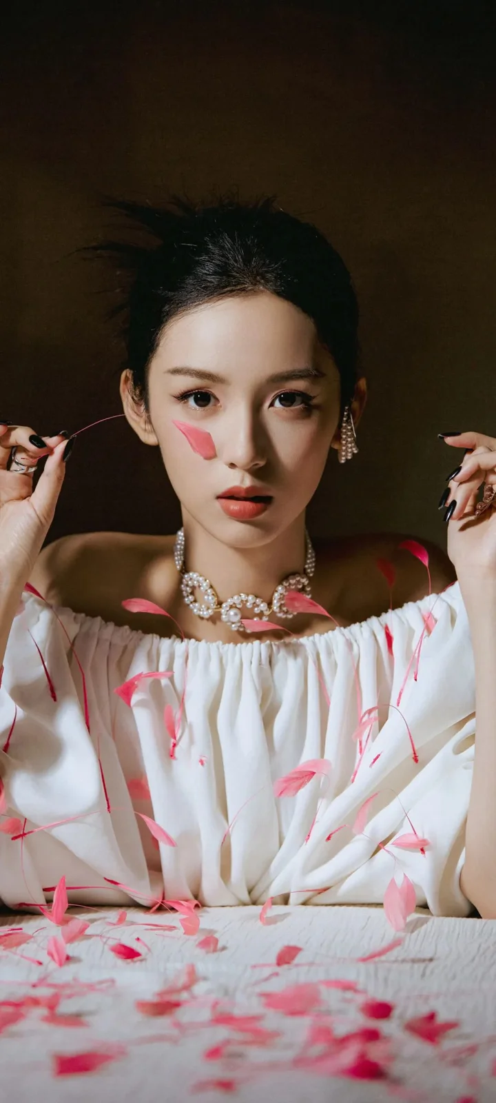 一位成年女性身穿白色露肩服装，手持细线，周围散落着粉色花瓣并佩戴华丽项链。