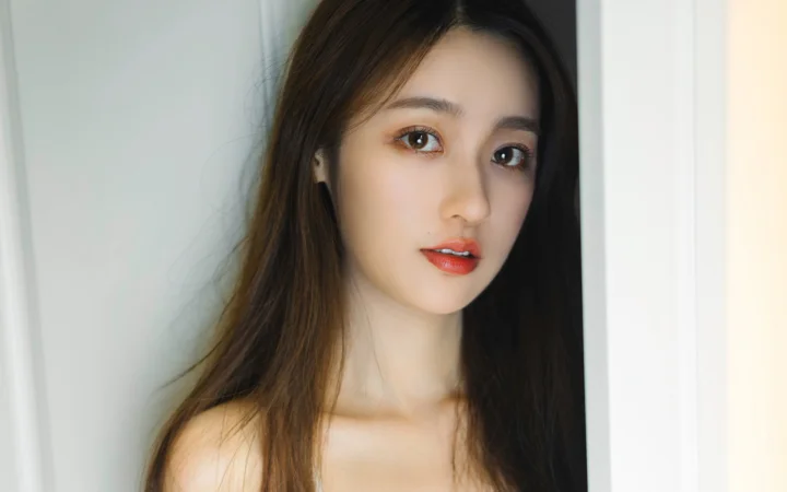 一名长发女性靠近明亮的窗边，面向镜头拍摄肖像。