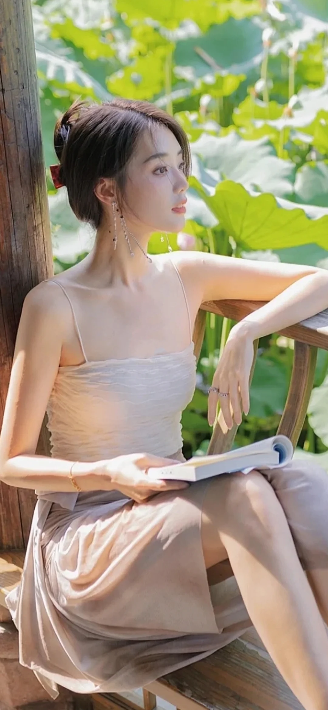 一名女子坐在木质阳台上，手持一本书，身后是明亮的绿色叶片。
