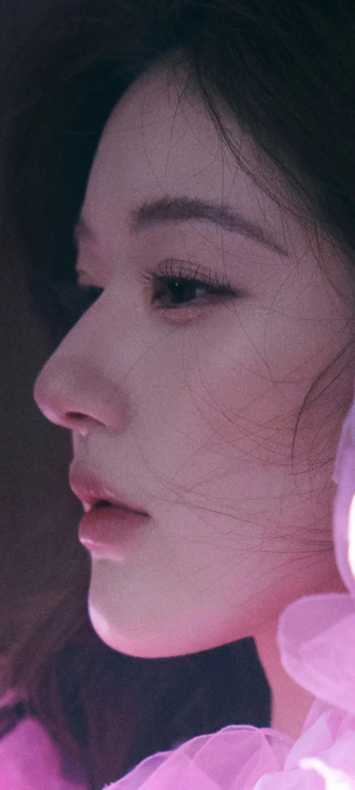 一位女性的侧脸近距离特写被柔和的粉紫色光线照亮。