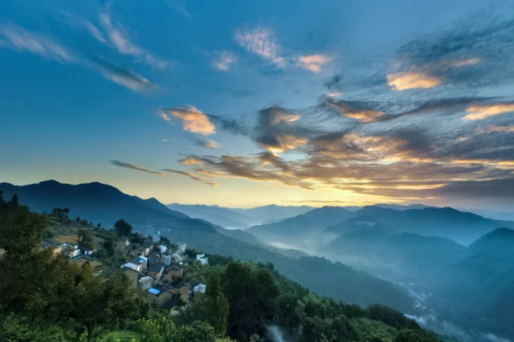 夕阳映照下的群山、森林与山间村落构成宁静的自然景色。