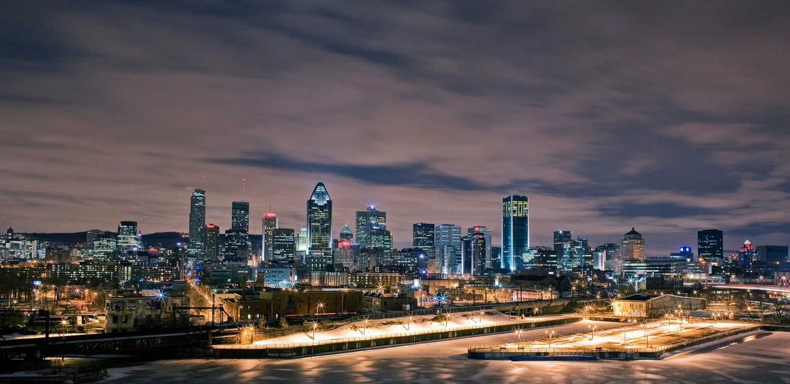 夜幕下的城市天际线灯火通明，前景道路与桥梁延伸至高楼之间。
