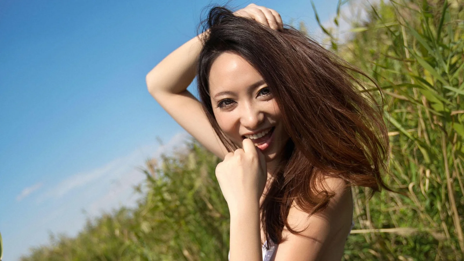 푸른 하늘 아래 갈대 옆에서 포즈를 취하는 성인 여성.