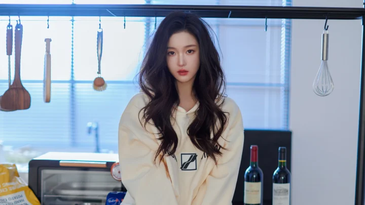 긴 머리의 여성이 조리 도구와 오븐, 와인병이 보이는 주방에 서 있습니다.