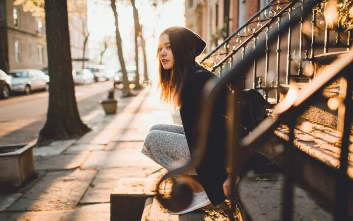 一名女子坐在城市街边的台阶旁，沐浴在温暖的阳光中。